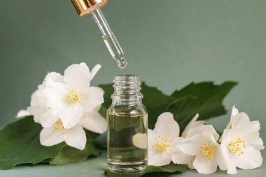 Yeşil arka planda yasemin çiçekleri olan gerekli yağlar için kozmetik cam şişe. Spa Doğal Serumları. Düşüren Şişe Model. Boşluğu kopyala