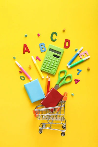 Carrello pieno di colorati materiali scolastici su sfondo giallo. Educazione, Ritorno a scuola, Shopping. — Foto Stock