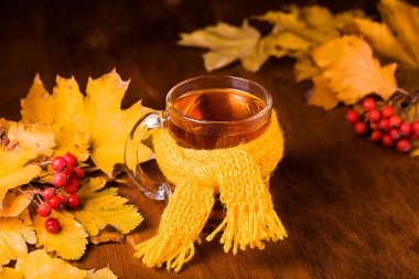 Sonbahar yapraklı bir eşarba sarılmış bir fincan çay, ahşap bir masada Rowan. Sağlığın için iyi..