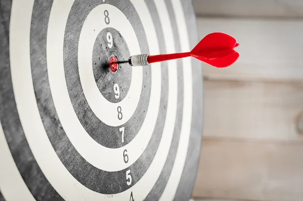 Red dart arrow hitting in the target center of dartboard