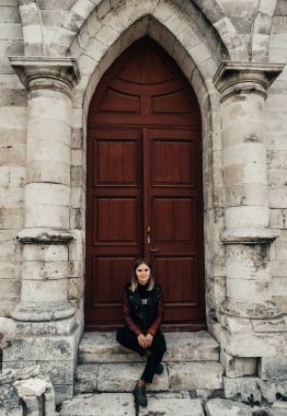 Gotik bir tapınağın antik ahşap kapısının girişinde deri ceketli genç bir kadın.