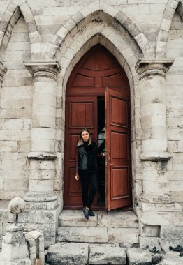Gotik bir tapınağın antik ahşap kapısının girişinde deri ceketli genç bir kadın.