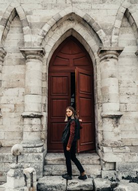 Gotik bir tapınağın antik ahşap kapısının girişinde deri ceketli genç bir kadın.