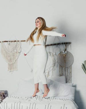 Yatak odasındaki beyaz tonlarda, uzun sarı saçlı, uzun, lüks bir kadın.