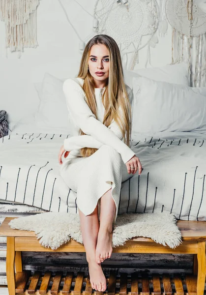 Молода жінка з довгим розкішним світлим волоссям на ліжку в спальні в інтер'єрі білих тонів — стокове фото
