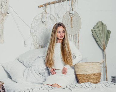 Yatak odasındaki beyaz tonlarda, uzun sarı saçlı, uzun, lüks bir kadın.