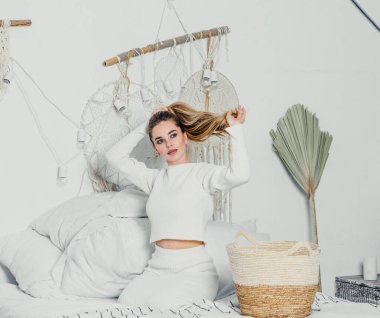 Yatak odasındaki beyaz tonlarda, uzun sarı saçlı, uzun, lüks bir kadın.