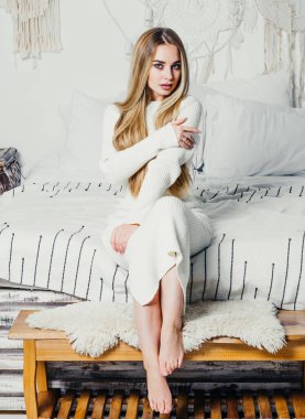 Yatak odasındaki beyaz tonlarda, uzun sarı saçlı, uzun, lüks bir kadın.