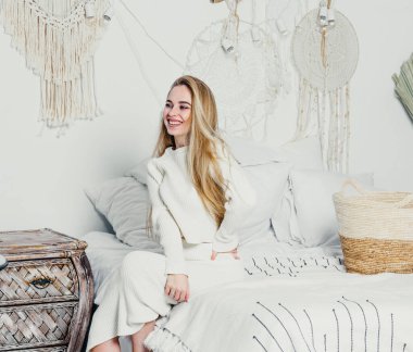 Yatak odasındaki beyaz tonlarda, uzun sarı saçlı, uzun, lüks bir kadın.