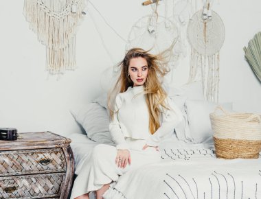 Yatak odasındaki beyaz tonlarda, uzun sarı saçlı, uzun, lüks bir kadın.