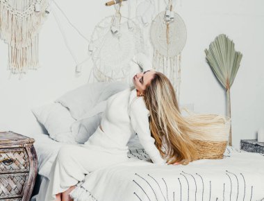 Yatak odasındaki beyaz tonlarda, uzun sarı saçlı, uzun, lüks bir kadın.