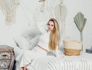 Yatak odasındaki beyaz tonlarda, uzun sarı saçlı, uzun, lüks bir kadın.