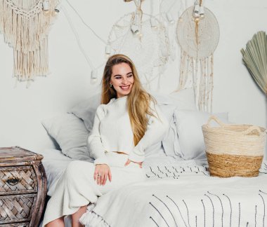 Yatak odasındaki beyaz tonlarda, uzun sarı saçlı, uzun, lüks bir kadın.