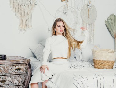 Yatak odasındaki beyaz tonlarda, uzun sarı saçlı, uzun, lüks bir kadın.