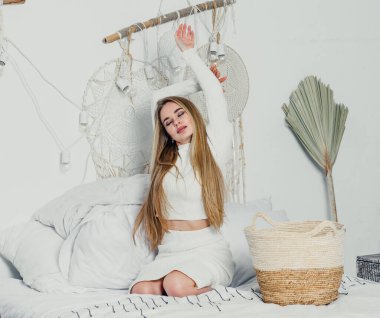 Yatak odasındaki beyaz tonlarda, uzun sarı saçlı, uzun, lüks bir kadın.