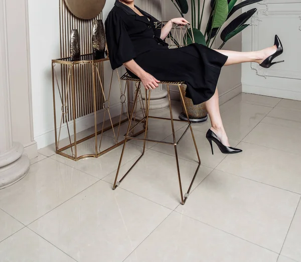 Junge elegante Frau im schwarzen Kleid mit Knöpfen sitzt auf einem eisernen Stuhl schöne lange Beine schlank — Stockfoto