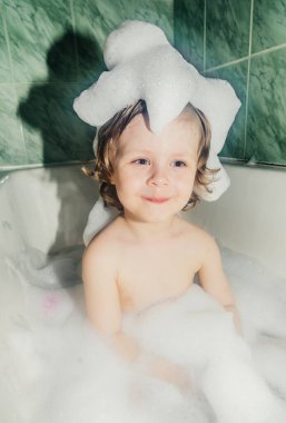 Güzel çocuk çocuk banyo oyunlarında yıkanır sabun köpükleri ve köpüklerle eğlenir.