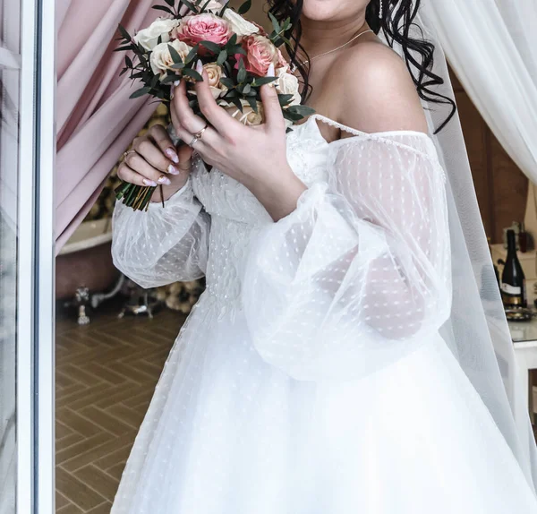 Jeune belle mariée dans une robe de mariée élégante et délicate blanche avec un bouquet de fleurs rose — Photo