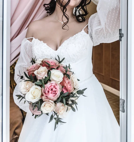 Jeune belle mariée dans une robe de mariée élégante et délicate blanche avec un bouquet de fleurs rose — Photo