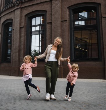 Uzun saçlı, çocuklu, genç ve güzel bir anne. Sokakta yürürken mutluluk, eğlence ve annelik.