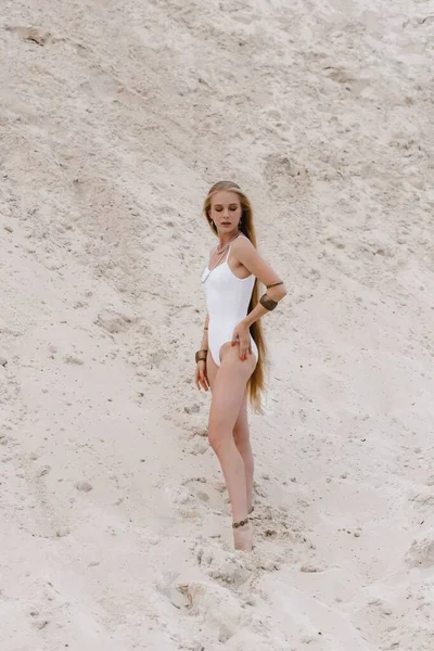 Young slender beautiful slim sexy woman in white swimwear bodysuit on white sand on the beach with — Stock Photo, Image