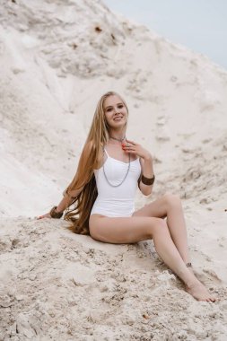 Genç, zayıf, güzel, beyaz mayo giyen seksi kadın kumsalda beyaz bir kumda mayo giyiyor.