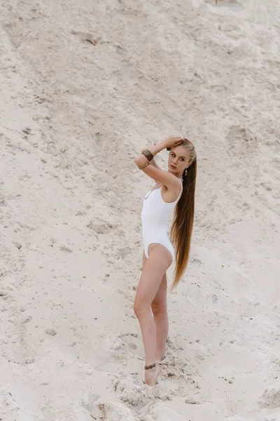 Young slender beautiful slim sexy woman in white swimwear bodysuit on white sand on the beach with — Stock Photo, Image