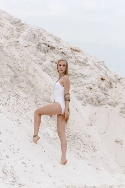 Young slender beautiful slim sexy woman in white swimwear bodysuit on white sand on the beach with — Stock Photo, Image