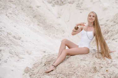 Genç, zayıf, güzel, beyaz mayo giyen seksi kadın kumsalda beyaz bir kumda mayo giyiyor.