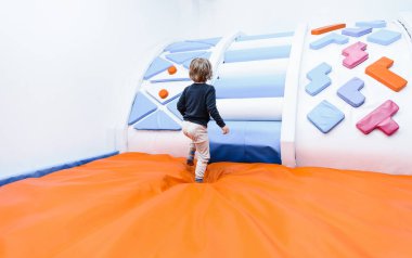 Oğlan çocuk şişme trambolinlerle çocuk odasında oynuyor, kaydırak aktif oyuna tırmanıyor.