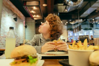 Aç çocuk restoranda hamburger yiyor