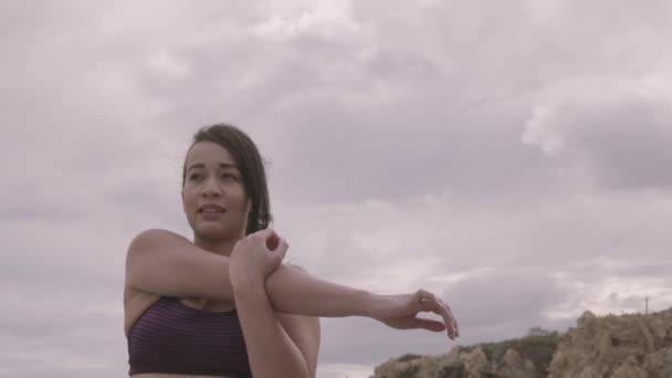 Mujer joven ejercitándose en la playa con el tiempo nublado. Estiramiento. Fitness. Moción lenta — Vídeos de Stock