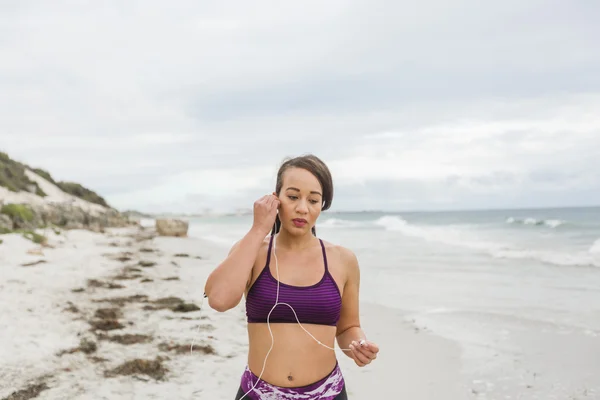 Corredor femenino preparándose para el entrenamiento al aire libre en la playa configurando auriculares — Foto de Stock
