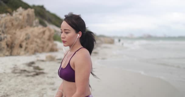 Νεαρή γυναίκα ευτυχισμένη μετά τζόκινγκ στην παραλία στη συννεφιά. Γυμναστήριο. Αργή κίνηση — Αρχείο Βίντεο