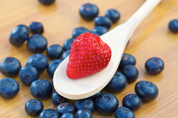 Strawberry on a wooden spoon with blueberries — Stock Photo, Image