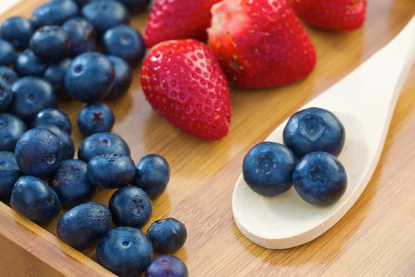 Blueberries on wooden spoon with strawberries — Stock Photo, Image