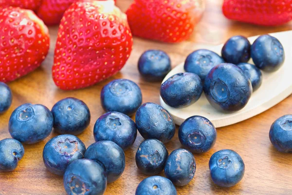 Blueberries on wooden spoon with strawberries — Stock Photo, Image