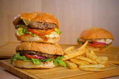 Eritilmiş peynir ve kalın etli zemin sığır patty, marul, domates, soğan, ahşap masa üzerinde duran susam çörek ile lezzetli hamburger