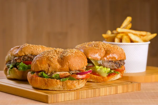 Hamburger savoureux au fromage fondu et épaisse galette de poulet haché succulent, laitue, tomate, oignon, pain au sésame debout sur une table en bois — Photo