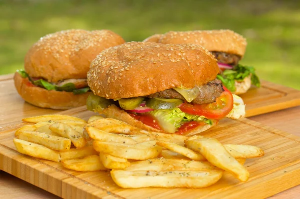 Hamburger savoureux au fromage fondu et épaisse galette de boeuf haché succulente, laitue, tomate, oignon, pain de sésame debout sur une table en bois — Photo