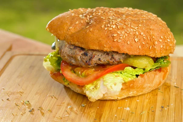 Tasty burger with melted cheese and thick succulent ground beef patty, lettuce, tomato, onion, sesame bun standing on wooden table — Stock Photo, Image