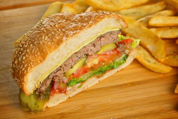 Hamburger tagliato con formaggio fuso e carne di manzo macinata succulenta spessa, lattuga, pomodoro, cipolla, panino di sesamo in piedi su tavolo di legno — Foto Stock