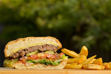 Eritilmiş peynir ve kalın etli zemin sığır patty, marul, domates, soğan, ahşap masa üzerinde duran susam çörek ile düzenlenen burger