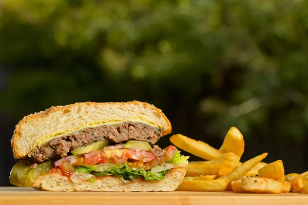 Burger tăiat cu brânză topită și carne de vită suculentă groasă, salată verde, roșii, ceapă, coc de susan în picioare pe masă de lemn — Fotografie, imagine de stoc