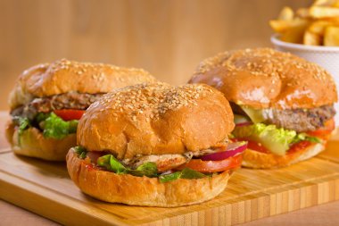 Eritilmiş peynir ve kalın etli kara tavuk patty, marul, domates, soğan, ahşap masa üzerinde duran susam çörek ile lezzetli burger