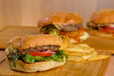 Eritilmiş peynir ve kalın etli zemin sığır patty, marul, domates, soğan, ahşap masa üzerinde duran susam çörek ile lezzetli burger