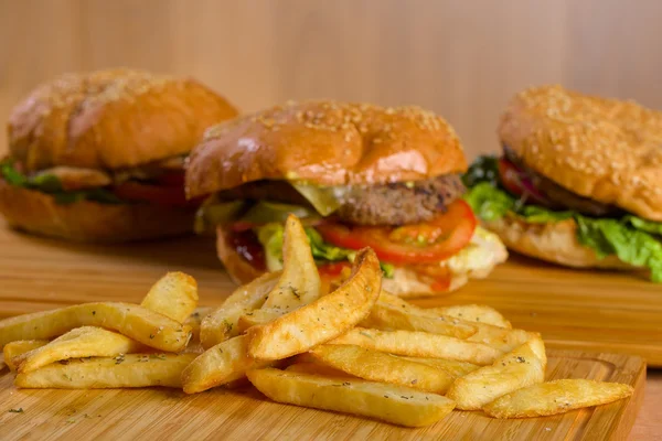 Patatas fritas con sabrosas hamburguesas frescas de pie sobre tabla de madera — Foto de Stock