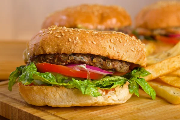 Sabrosa hamburguesa con queso derretido y carne molida suculenta gruesa empanada, lechuga, tomate, cebolla, pan de sésamo de pie sobre una mesa de madera — Foto de Stock