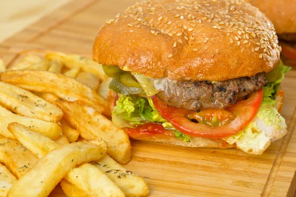 Sabrosa hamburguesa con queso derretido y carne molida suculenta gruesa empanada, lechuga, tomate, cebolla, pan de sésamo de pie sobre una mesa de madera — Foto de Stock