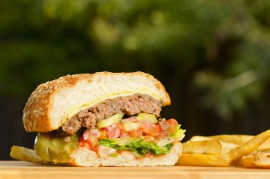 Eritilmiş peynir ve kalın etli zemin sığır patty, marul, domates, soğan, ahşap masa üzerinde duran susam çörek ile düzenlenen burger